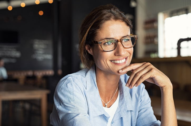 A middle aged woman in glasses at a coffee shop smiling.
