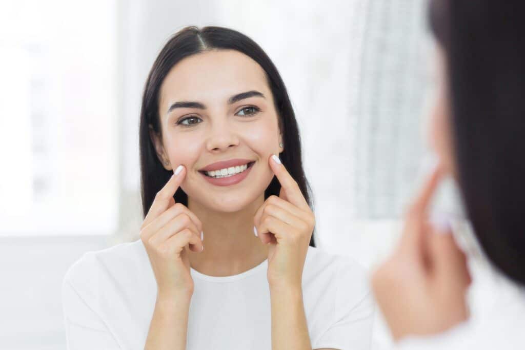 A woman looking in the mirror after receiving non-invasive skin treatments in Boca Raton.