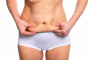 A woman in white underwear pinching fat on her lower stomach