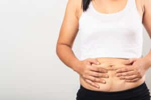 Closeup of woman pulling on loose stomach skin, considering a tummy tuck.