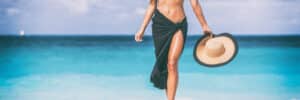 Woman walking on beach in swimsuit cover up showing beautiful legs after thighlift