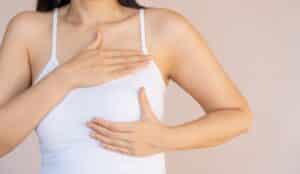Woman in tank top cupping one of her reconstructed breasts