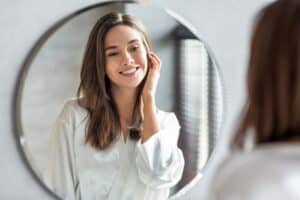 Woman smiling at herself in the mirror, happy with the results from her Juvederm treatment.