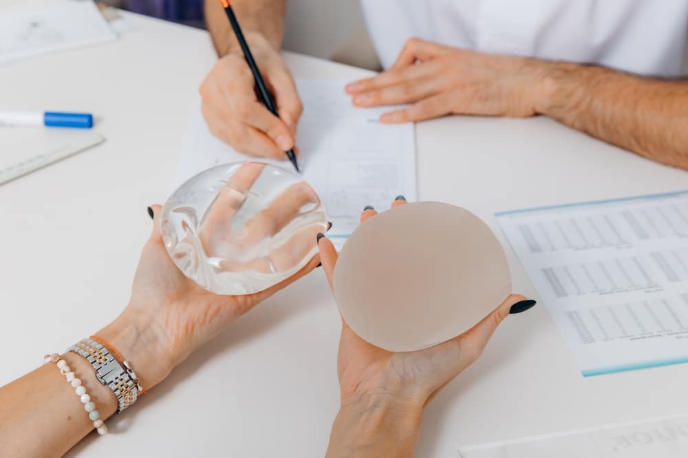 Woman holding two different types of implants in a consultation with a plastic surgeon.