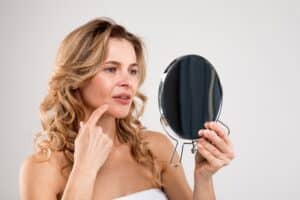 Middle-aged woman examining her face in a handheld mirror, considering cosmetic treatments like BOTOX